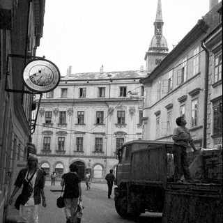 Historic European street scene with pedestrians, old architecture, and vintage truck.