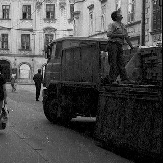 Historic European street scene with pedestrians, old architecture, and vintage truck.