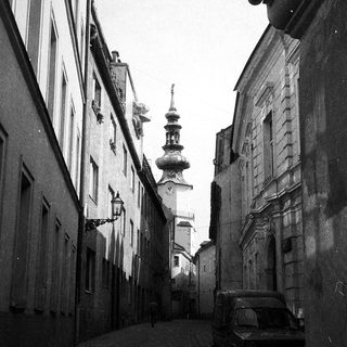 Narrow European street with historic buildings, cobblestones, and church tower.