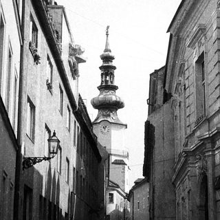 Narrow European street with historic buildings, cobblestones, and church tower.