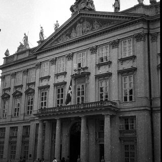 Baroque-style palace entrance with statues and flag.