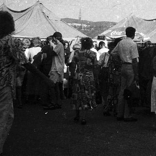 Outdoor market with clothing stalls and crowd.