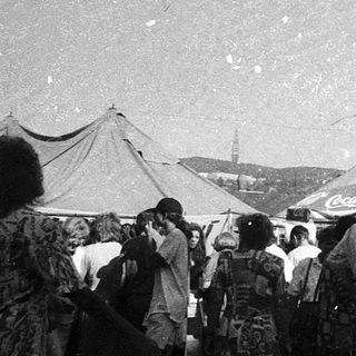 Outdoor market with clothing stalls and crowd.