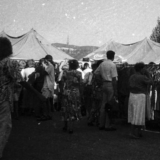 Outdoor market with clothing stalls and crowd.