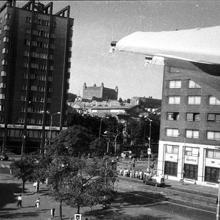 Urban scene with castle in background, mid-20th century buildings.
