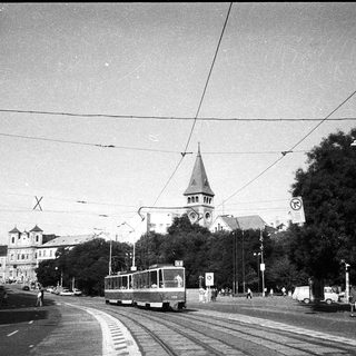 Urban street scene with tram, historic church, and pedestrians.