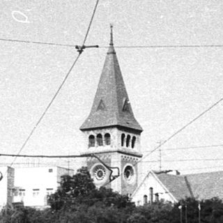 Urban street scene with tram, historic church, and pedestrians.