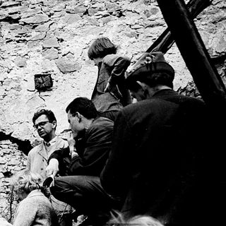 Ruins with people inspecting earthquake-damaged stone structure.