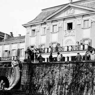Historic building with crowd on balcony near water.