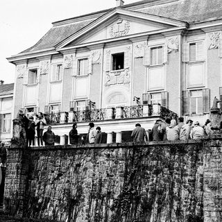 Historic building with crowd on balcony near water.