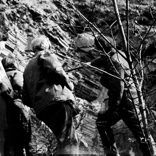 Two men examining exposed rock layers outdoors.