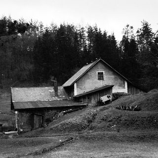 Rural farmhouse with attached barn on hilly terrain.