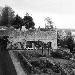 Historic stone building with formal gardens overlooking river.