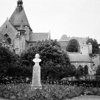 Historic castle with bust monument in landscaped garden.
