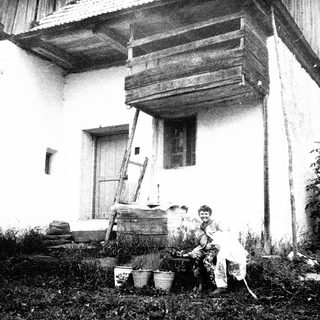 Rural woman tending garden near traditional wooden house.