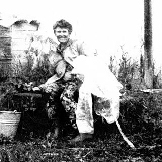 Rural woman tending garden near traditional wooden house.