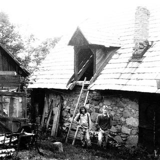 Rural scene with two men near rustic stone house and wooden ladder.