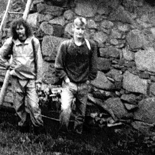 Rural scene with two men near rustic stone house and wooden ladder.