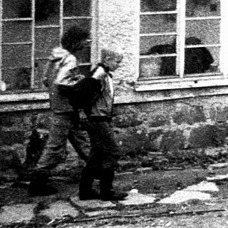 People gathering outside damaged building during cleanup.