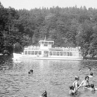 People swimming and boating near a docked ferry.