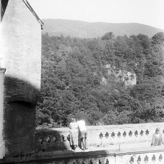 Couple walking on historic stone balcony overlooking forested hills.
