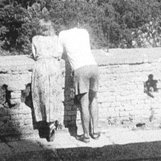 Couple walking on historic stone balcony overlooking forested hills.
