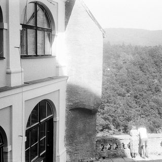 Historic building exterior with people on balcony overlooking lush landscape.