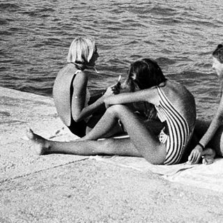 Three people sitting by waterfront on sunny day.