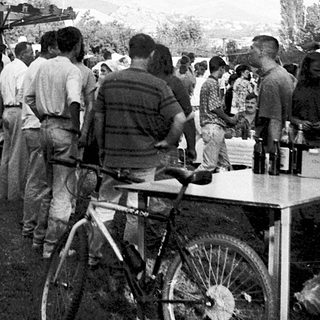 Crowded outdoor gathering with large flags and tables.