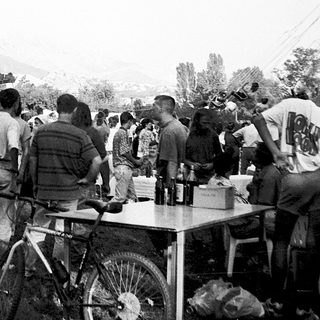 Crowded outdoor gathering with large flags and tables.
