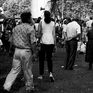 Crowded outdoor gathering with large flags and tables.