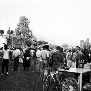 Crowded outdoor gathering with large flags and tables.