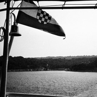Maritime bell and Croatian flag near water.