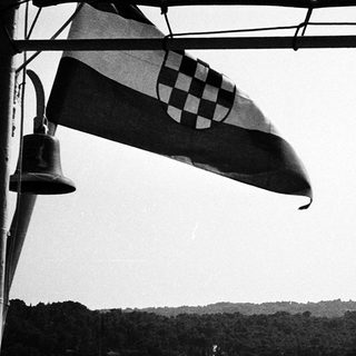 Maritime bell and Croatian flag near water.