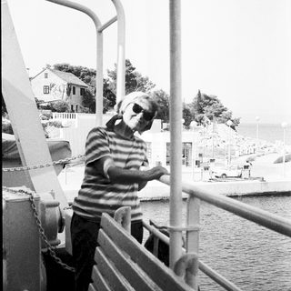 Person standing on ferry railing by water.