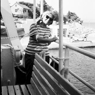 Person standing on ferry railing by water.