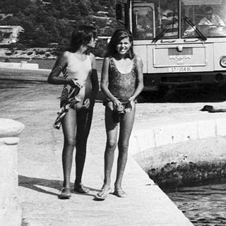 Two women by waterfront with boats and ferry.
