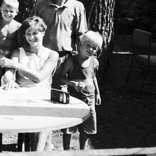 Family gathering outdoors around picnic table.