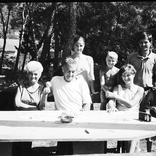 Family gathering outdoors around picnic table.