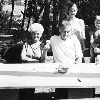 Family gathering outdoors around picnic table.