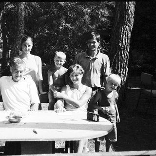 Family gathering outdoors around picnic table.