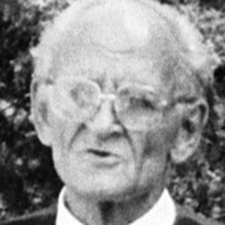 Elderly man standing outdoors in vintage vest and tie.