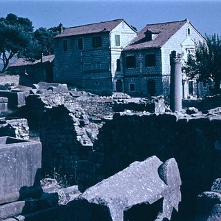 Ancient ruins with standing columns and modern buildings nearby.