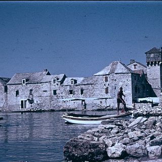 Historic stone buildings by waterfront with small boat.