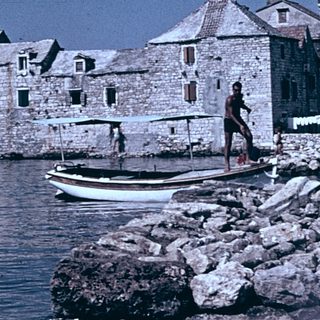 Historic stone buildings by waterfront with small boat.