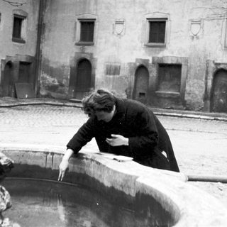 Person drinking from a snow-covered fountain in courtyard.