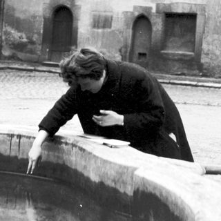 Person drinking from a snow-covered fountain in courtyard.