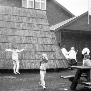 People playing frisbee outdoors near wooden structure.