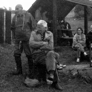 Group of people gathered outdoors near rustic shelter.
