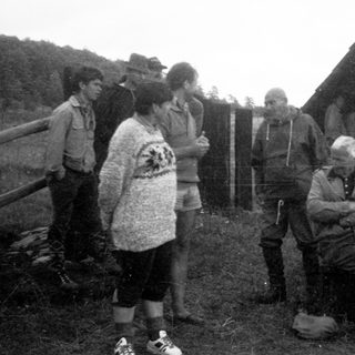 Group of people gathered outdoors near rustic shelter.